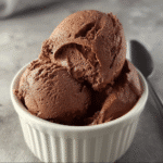 High-protein chocolate ice cream scoops in a white ramekin on gray background.