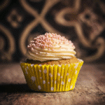 Frosted keto cupcake in yellow polka dot wrapper with ornate dark background