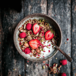 Final serving of High Protein Granola Recipe with crunchy clusters, yogurt, strawberries, and raspberries in a ceramic bowl.