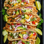 A tray of keto tacos with vibrant toppings and lime wedges