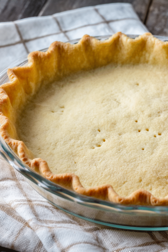 Golden baked easy keto pie crust in a glass pie dish on a cloth napkin