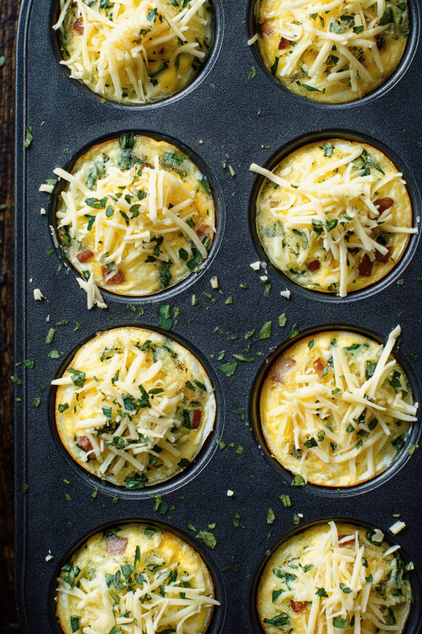 Preparing Bacon Egg And Cheese Muffins in Muffin Tin Bacon Egg And Cheese Muffins in a muffin tin with cheese and herbs on top
