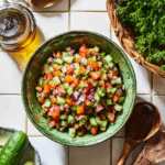 Colorful Arabic salad in a green bowl surrounded by cucumbers and parsley